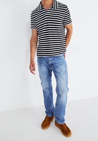 Koszulka polo w paski w kolorze czarnym i białym, z krótkimi rękawami i kołnierzykiem. Zestawiona z jasnoniebieskimi dżinsami i brązowymi butami wsuwanymi. Gładka faktura.