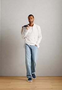 Hüübin outfit, mis koosneb valgest T-särgist, helesinistest teksadest ja tumehallidest spordijalatsitest. Ühe õla peal on kerge värviga särk.