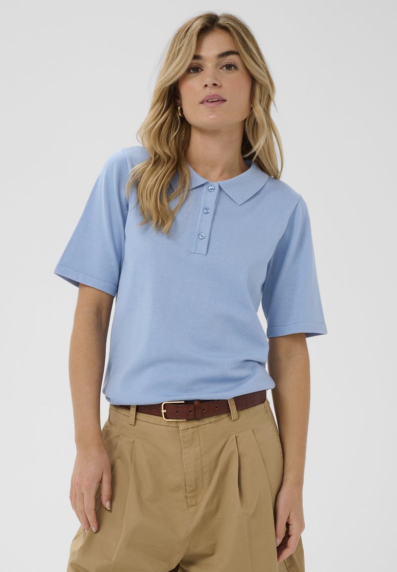 Polo bleu clair à manches courtes, avec une patte de boutonnage à trois boutons et un col, assorti à un pantalon kaki et une ceinture marron.