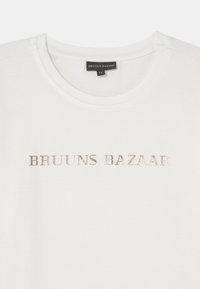 T-shirt de algodão branco com gola redonda e texto metálico em rosé dourado a dizer "BRUUNS BAZAAR" na parte da frente. Textura suave, design simples.