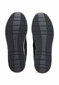 Suelas de calzado atlético negro con una parte inferior de goma texturizada. Presenta un patrón ondulado y nervaduras para el agarre, junto con secciones planas para la estabilidad.