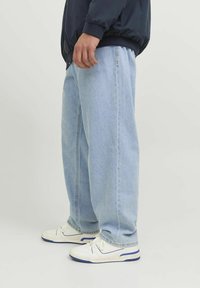 Ljusblå denimjeans med lös passform, rakt skurna och med synliga sömmar, ihop med vita sneakers med blå accenter.