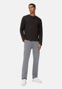 Sort langærmet henley skjorte med tre-knaps placket, parret med grå denim jeans og hvide sneakers. Enkel, afslappet outfit design.