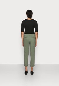 Pantaloni verde oliva con vestibilità affusolata e orli arrotolati, realizzati in tessuto leggero. Abbinati a una maglia nera aderente. Scarpe nere.