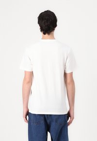 Weißes kurzärmeliges T-Shirt aus Baumwolle mit klassischem Rundhalsausschnitt und lockerer Passform, kombiniert mit blauen Jeans.
