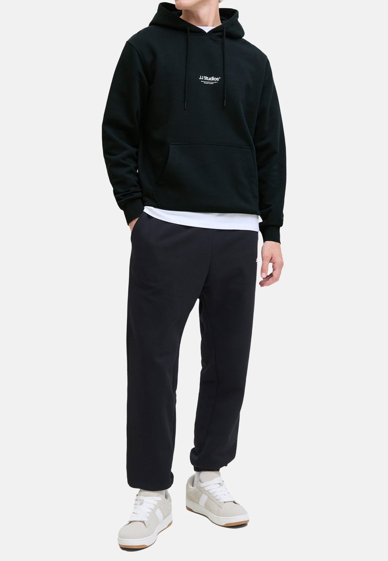 Sort hoodie med snore, frontlomme og logo. Sammen med mørke joggebukser og hvide sneakers. Enkel, afslappet og komfortabelt design.