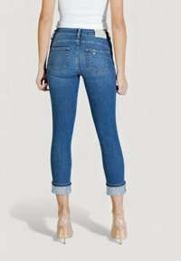 Siniset farkkuhousut kapeilla lahkeilla ja keskikorkealla vyötäröllä, käännettävät lahkeet joissa vaaleansininen yksityiskohta, sekä kaksi takataskua.