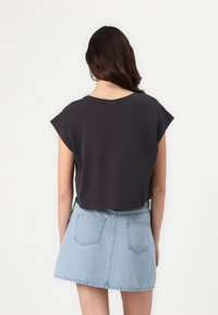 Sutrumpintas tamsiai pilkas T-shirt su trumpomis rankovėmis, derinamas su šviesiai mėlynomis džinsinėmis mini sijonėmis, turinčiomis užpakalines kišenes ir platėjančia forma.