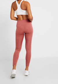Des leggings rose, ajustés, en tissu texturé, taille haute et au design sans couture, associés à des chaussures de sport blanches et un simple soutien-gorge de sport blanc.