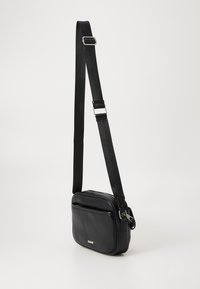 Borsa a tracolla nera in pelle con una texture liscia, forma rettangolare, tracolla in tessuto regolabile e tasca anteriore con zip.