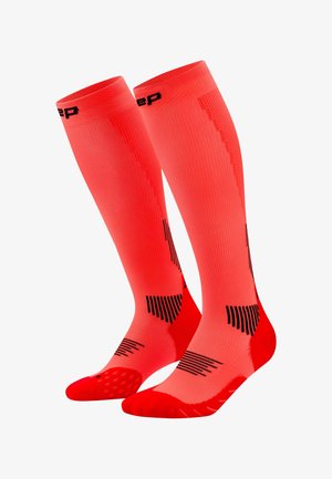 Pair of bright coral knee-high compression socks with black geometric accents and reinforced red heel and toe areas.