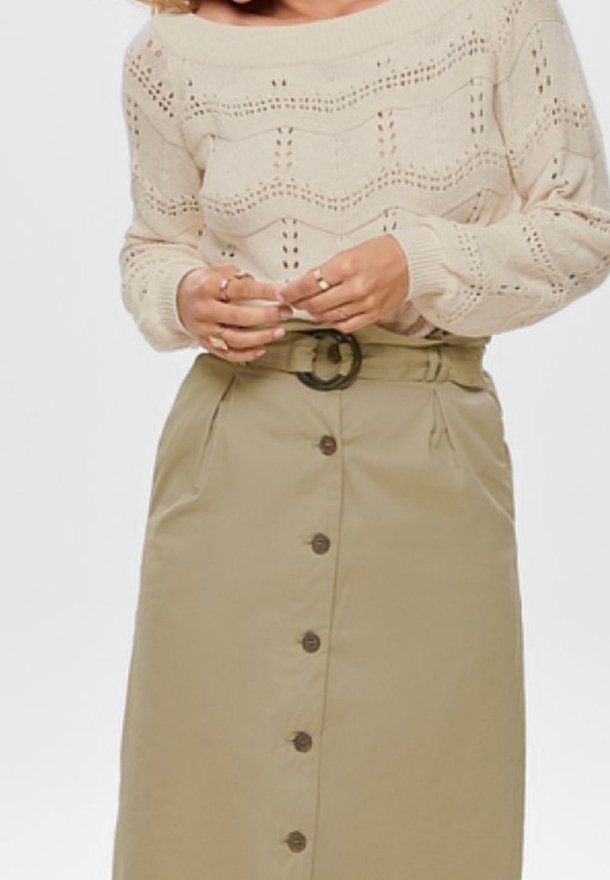Femme portant un pull en maille beige et une jupe taille haute kaki avec des boutons à l'avant et une boucle de ceinture ronde noire.