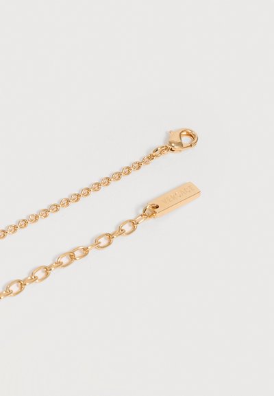Collier chaîne en or avec fermoir mousqueton et plaque rectangulaire gravée "VERSACE" sur fond blanc.