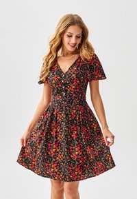 Robe fleurie noire ornée de fleurs orange vif et rose, manches courtes bouffantes, encolure en V, et jupe évasée avec boutons.