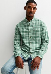 Groene geruite button-down blouse van een textuurstof, met houten knopen en een standaard kraag, gecombineerd met lichtblauwe jeans.
