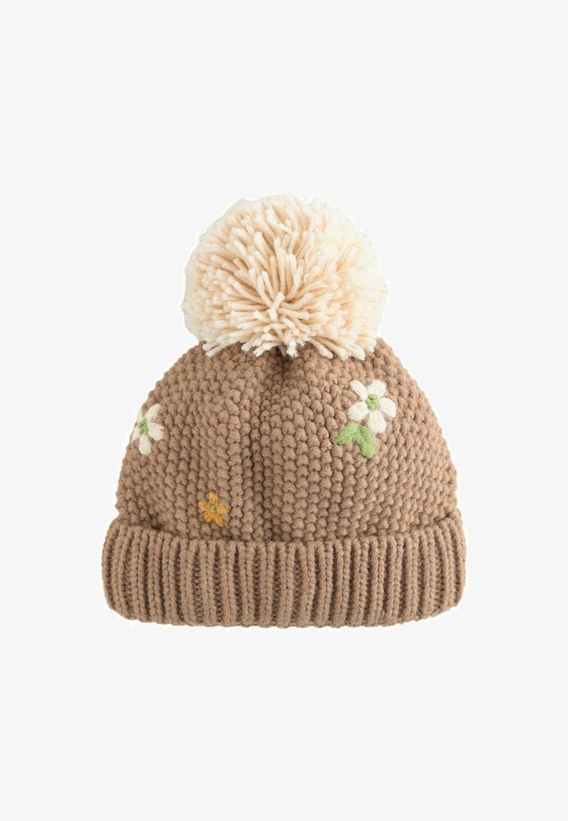 Bonnet en tricot marron avec un grand pompon beige duveteux sur le dessus, arborant des fleurs brodées en blanc, jaune et vert.