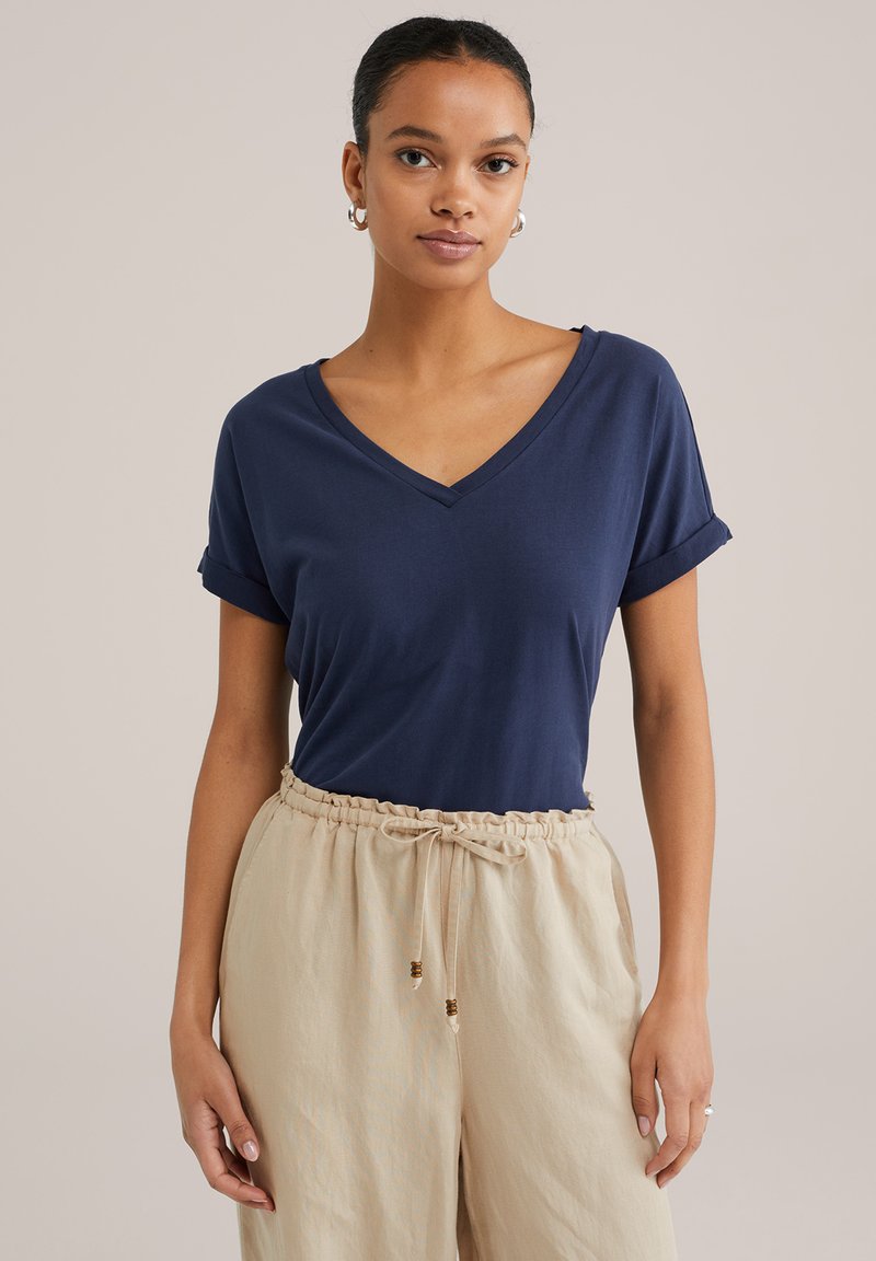 Jūras spēku V-veida krekls ar sarullētām piedurknēm, kas izgatavots no mīksta auduma. Kombinēts ar beigu krāsas biksēm ar aukliņu, kurām ir koka akcenti.