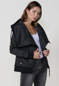 Felpa nera con motivo, dotata di un ampio colletto a strati, zip e polsini a costine. Presenta una texture del tessuto e un sottile dettaglio del logo vicino all'orlo.