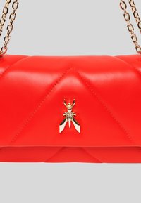 Borsa a tracolla in pelle rossa trapuntata con un accessorio in metallo a forma di ape dorata e una tracolla a catena, con una texture liscia e un design elegante.