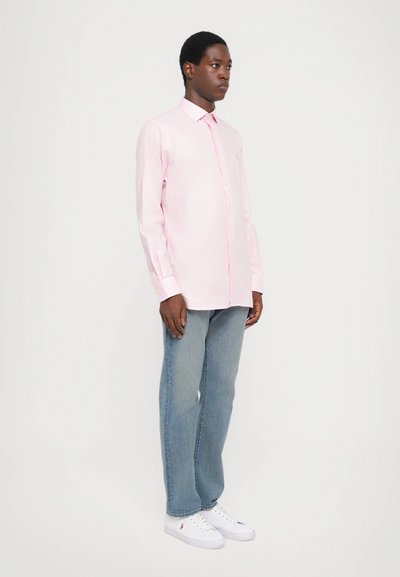 Ανοιχτό ροζ πουκάμισο με μακριά μανίκια και γιακά, σε συνδυασμό με μπλε τζιν και λευκά αθλητικά παπούτσια. Το πουκάμισο διαθέτει μια διακριτική καρό ύφανση.