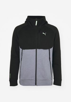 Sudadera negra y gris con cierre de cremallera, capucha y dos bolsillos laterales. Fabricada con una tela suave y con un acento de logo verde.