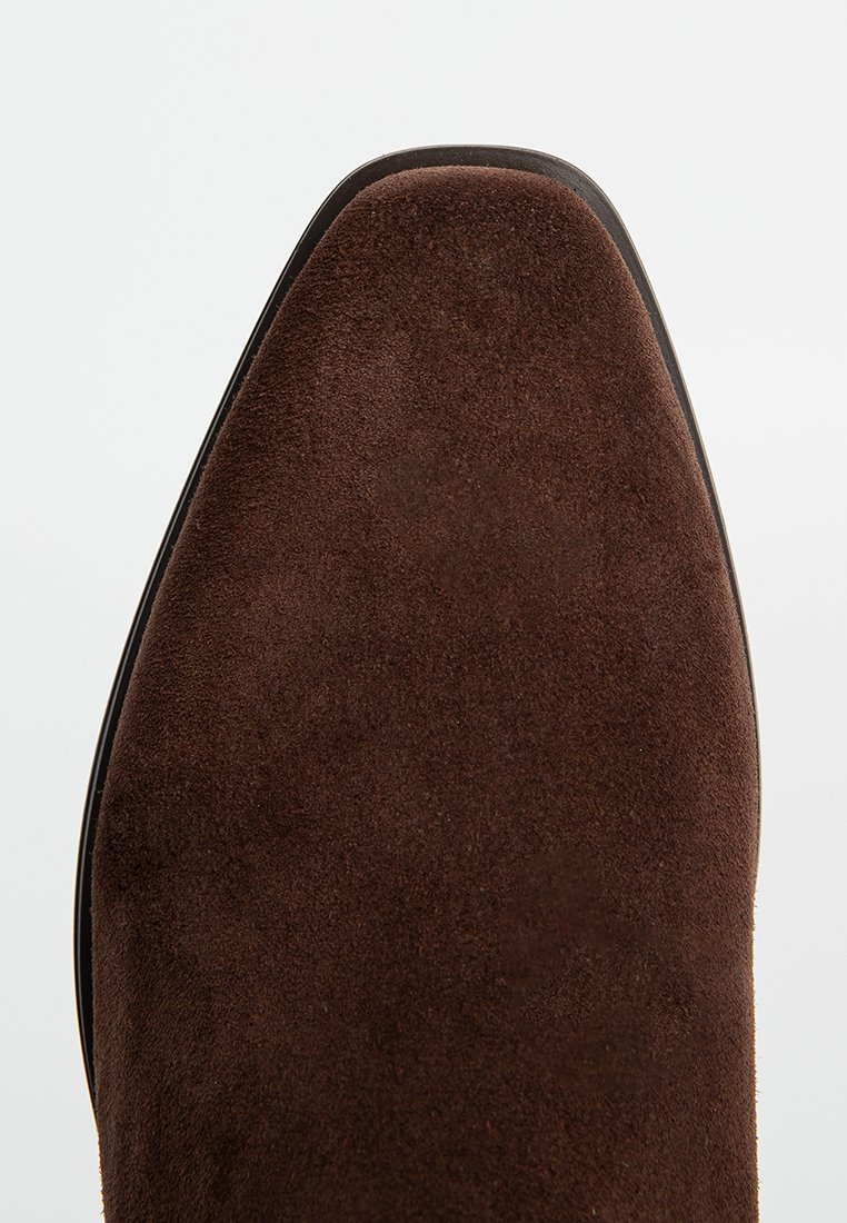 Braune Wildlederschuhe mit einer spitzen Zehenpartie und glatter schwarzer Sohle, die eine weiche Textur und klare Linien aufweisen.