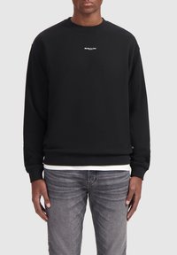 Zwarte sweatshirt van katoen, met een ronde hals, lange mouwen en een klein wit logo op de borst. Gecombineerd met grijze jeans.