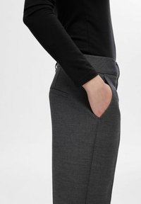 Pantalons gris ajustés en tissu texturé, dotés d'une poche latérale et d'un design slim, associés à un haut noir à manches longues.