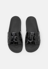 Par svart slidsandaler med strukturerade fotbäddar och blanka remmar präglade med stora "HUGO" bokstäver, visade ovanifrån på vit bakgrund.