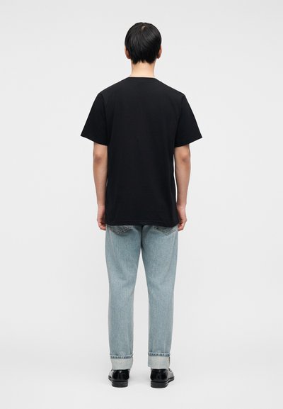 Μαύρο βαμβακερό μπλουζάκι με στρογγυλή λαιμόκοψη, συνδυασμένο με ανοιχτόχρωμο τζιν παντελόνι σε αν οιχτό μπλε, με γυρισμένα ρεβέρ και μαύρα παπούτσια. Απλός και καθημερινός σχεδιασμός.