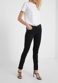 Vaqueros negros ajustados de talle alto, con costuras detalladas y cinco bolsillos, combinados con una camiseta blanca de manga corta sencilla y tacones negros.