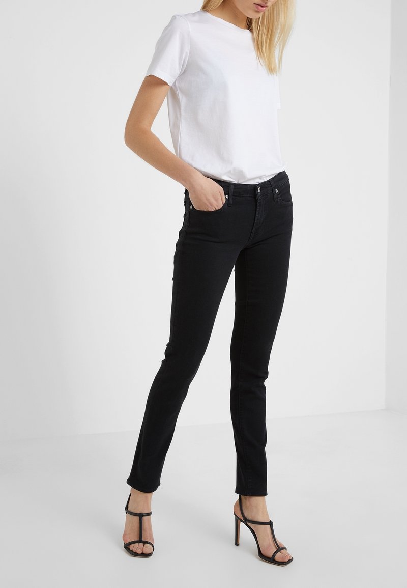 Vaqueros negros ajustados de talle alto, con costuras detalladas y cinco bolsillos, combinados con una camiseta blanca de manga corta sencilla y tacones negros.