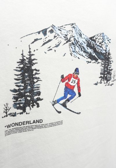 Biele tričko s potlačou lyžiara v červenom a modrom výstroji na pozadí zasneženej hory, pod ktorým je čierny nápis „WONDERLAND“.