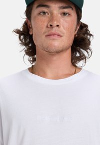 Weißes T-Shirt mit kurzen Ärmeln und gesticktem "Quiksilver"-Logo in Weiß. Weicher Stoff und runder Ausschnitt, körpernah am Hals.