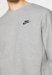 Felpa grigia realizzata in tessuto morbido, con logo Nike nero sul lato sinistro del petto e classico scollo rotondo.