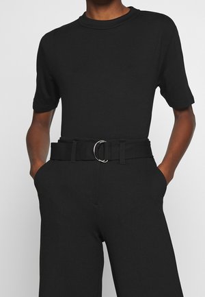 Czarna dopasowana koszulka z okrągłym dekoltem, połączona z czarnymi spodniami w wysokim stanie. Spodnie mają szeroki pasek z okrągłą srebrną klamrą.