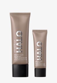Deux tubes de Smashbox Halo Healthy Glow Tinted Moisturizer, un grand et un petit, avec une finition beige mate et un texte argenté.