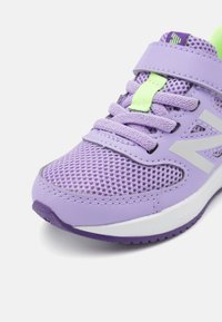 Bottines de sport violettes avec tige en mesh, accents verts contrastants, large semelle intermédiaire blanche et semelle extérieure texturée pour une meilleure adhérence.