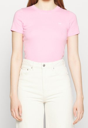 Różowa koszulka z krótkim rękawem, wykonana z miękkiej bawełny, z okrągłym dekoltem i małym logo na klatce piersiowej, zestawiona z białymi spodniami o wysokim stanie.