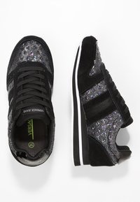 Baskets de sport noires avec dessus scintillant, accents en daim, design à lacets et semelle en caoutchouc blanche avec des rayures noires et blanches.