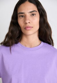 Short-sleeve t-shirt in light purple cotton, featuring a round neck and smooth texture. Details include a simple, classic design.