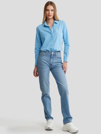 Camisa de botones a rayas azules con cuello, combinada con jeans azul claro y zapatillas blancas, con un corte relajado y un sutil detalle de bordado.