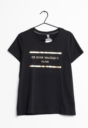 Sort kortærmet T-shirt på bøjle med guldtekst "CE SOIR MAGIQUE PARIS" indrammet af to gyldne vandrette linjer.