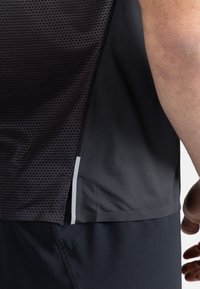 Černý sportovní top na ramínka s texturovanou horní částí s hexagonálním vzorem, hladkou spodní částí a bočním rozparkem pro ventilaci.