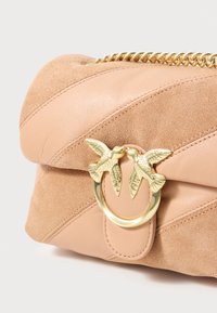  Bolsa crossbody em pele e camurça na cor rosa claro, com um detalhe de pássaro em tom dourado e uma alça em corrente. Painéis diagonais texturizados.