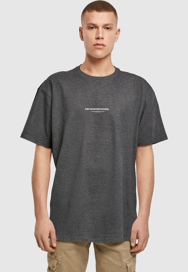 Mørkegrå oversized t-shirt lavet af bomuld, med korte ærmer og rund halsudskæring. Har hvid tekst "METAMORPHOSIS" på brystet.
