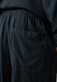 Donkerblauwe katoenen broeken hebben een elastische tailleband en een enkele achterzak met een rechthoekige vorm en gestikte randen.