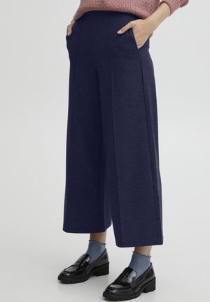 Marineblauwe wijde broeken met twee zijzakken, gemaakt van een zachte, gestructureerde stof, gecombineerd met zwarte instapschoenen en blauwe geribbelde sokken.