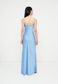 Vestido longo sem mangas em cetim azul, com um corte ajustado, apresenta alças ajustáveis e um pequeno fecho de botão nas costas.