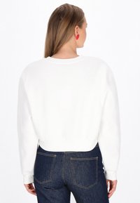 Hanorac alb scurt, cu guler rotund, manșete și bandă inferioară refiletate; asortat cu blugi din denim albastru închis.